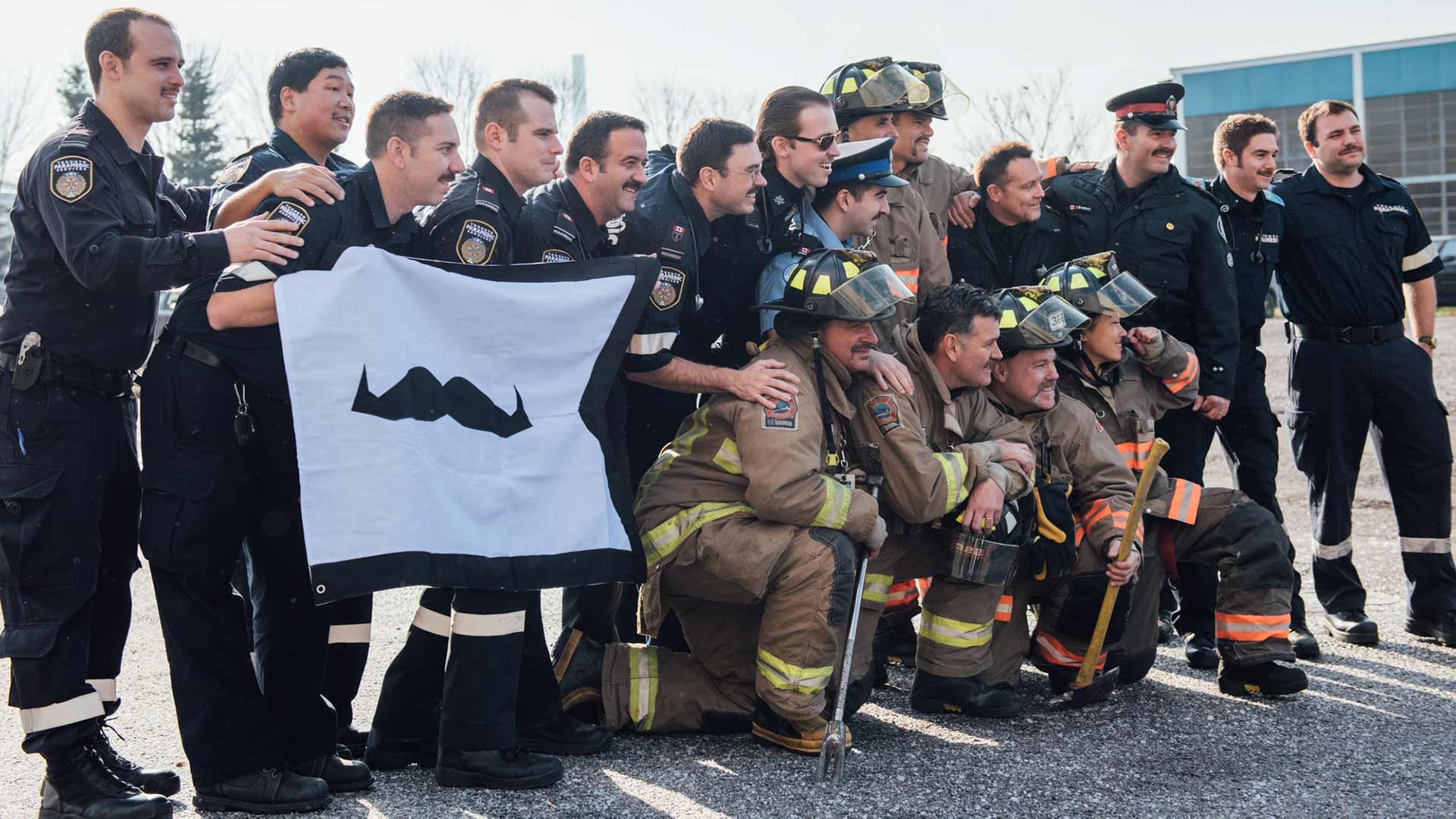 Photo of first responders posing to camera while holding a Movember-branded flag
