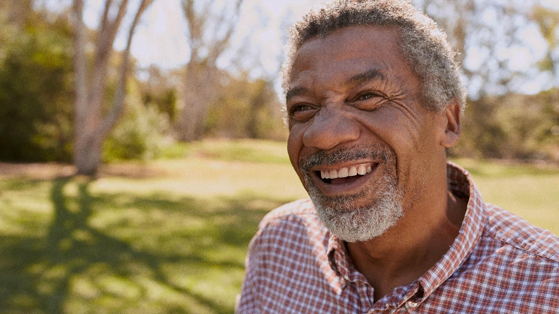 A mature-aged Black man smiling while looking past the camera.