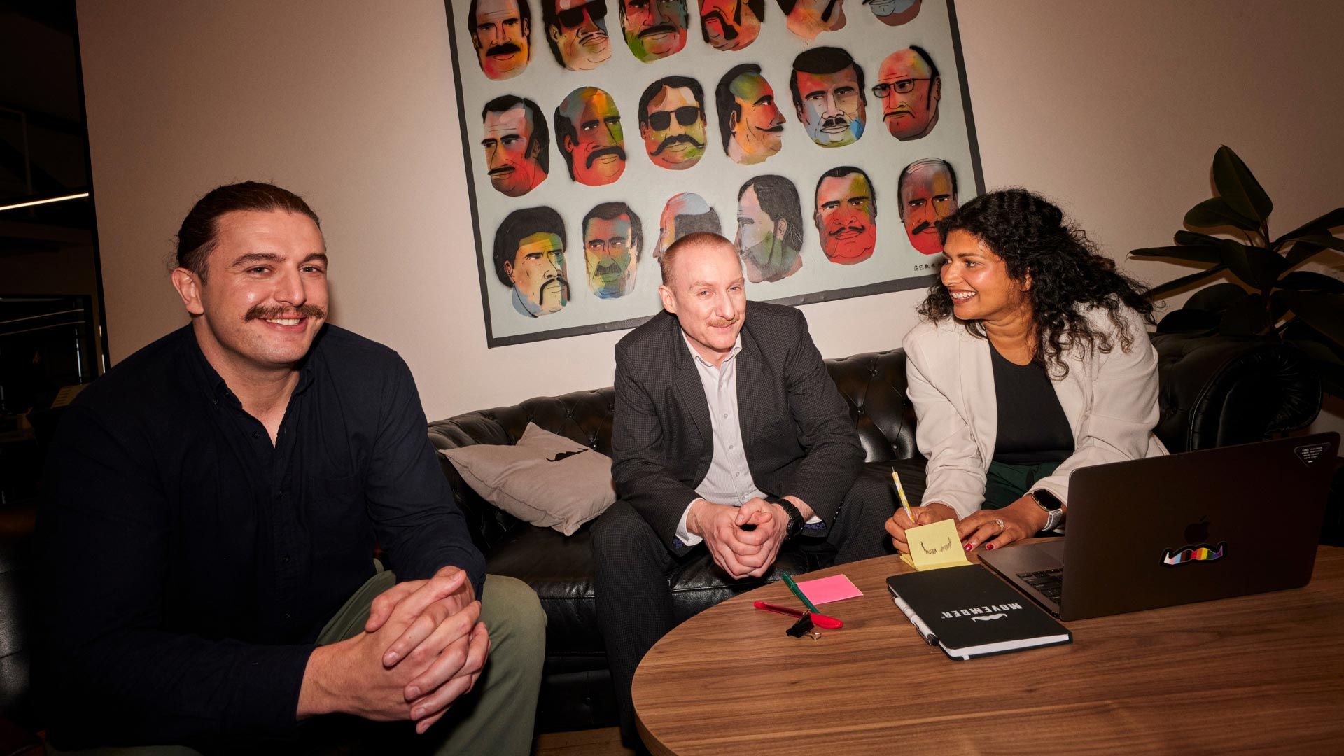 Photo showing three seated people in an office, smiling to camera.