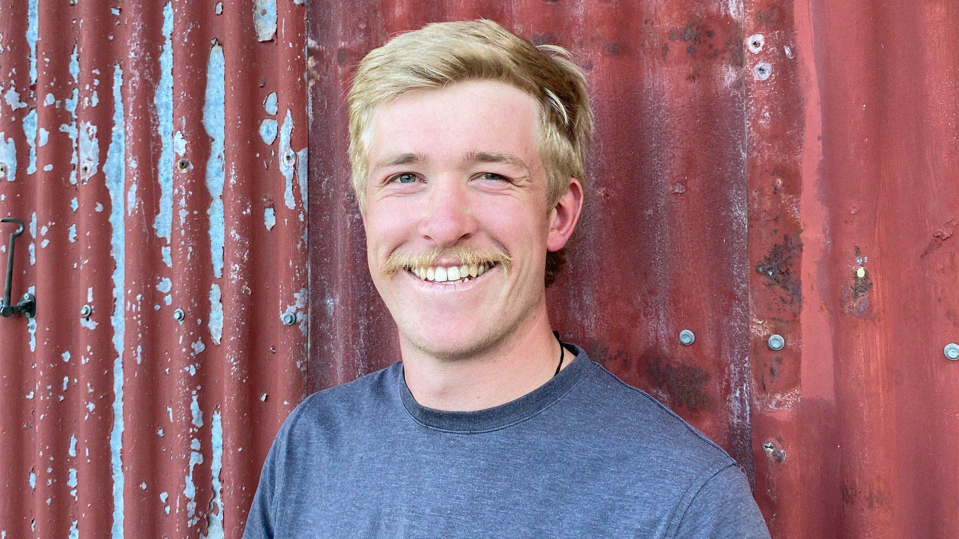 A moustachioed young man smiles for a portrait