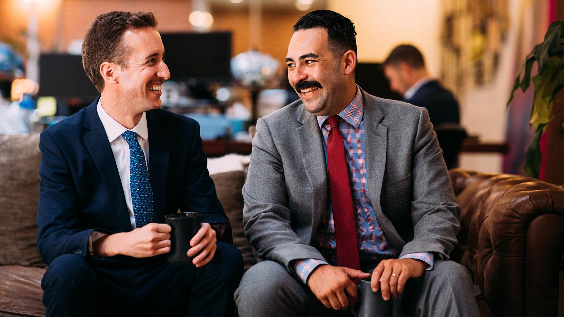 Photo showing two smiling, suited me in an office.